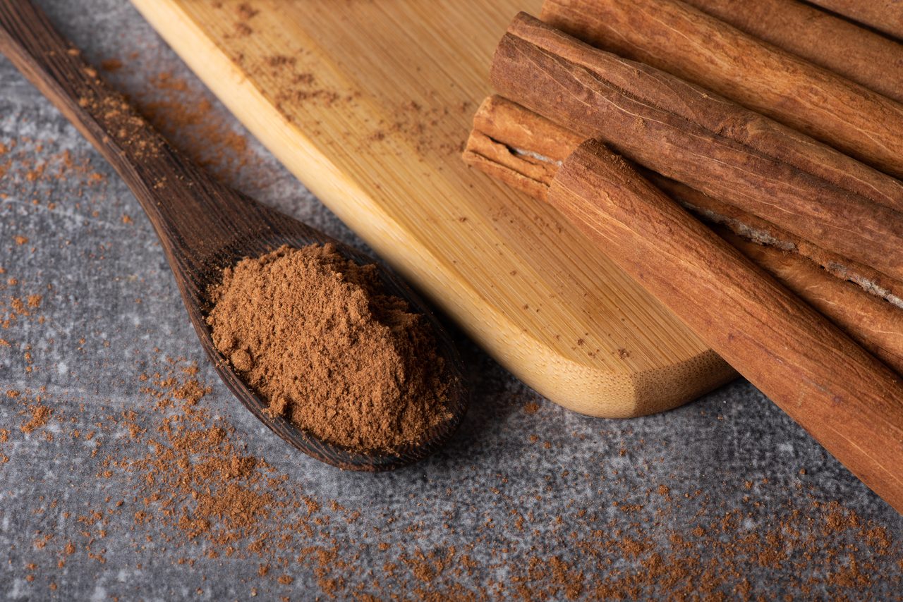 Canela en rama y molida en una cuchara sobre fondo de madera